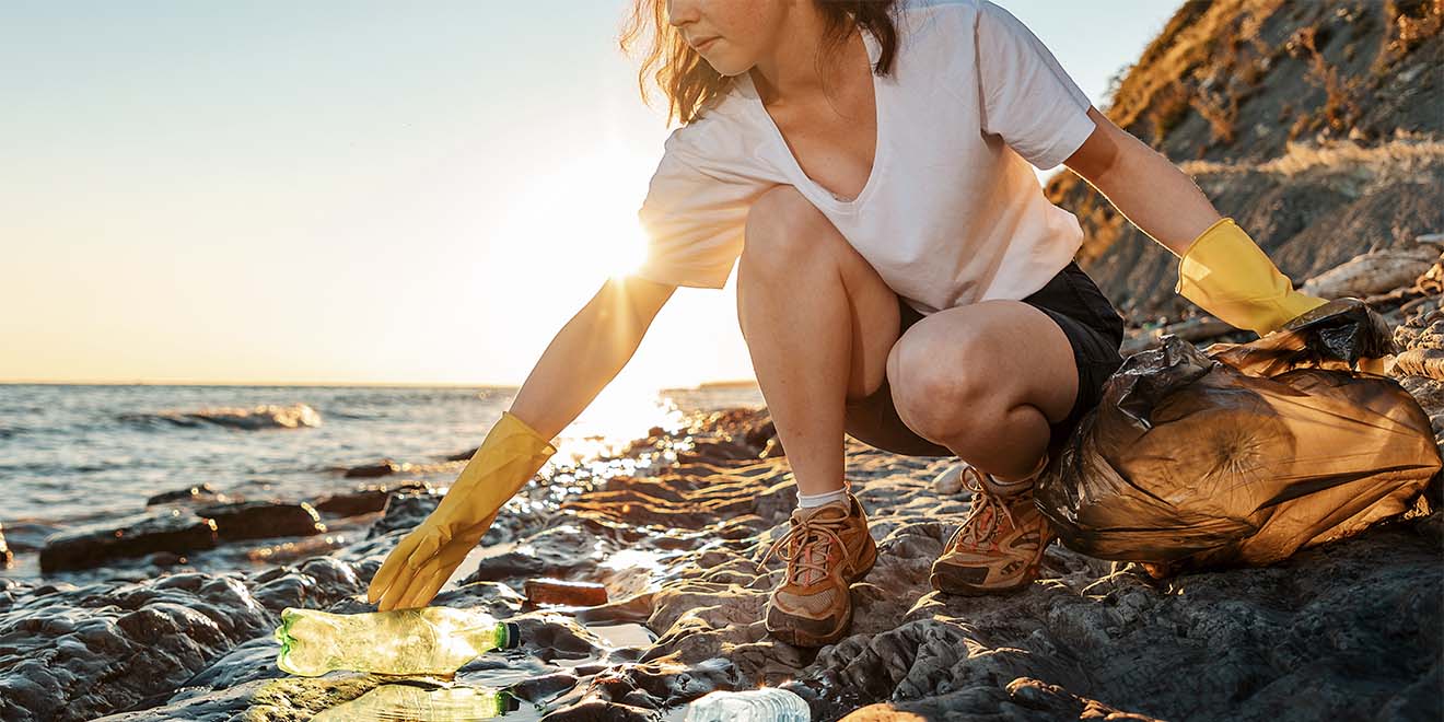 A young caucasian woman volunteer squats and picks up garbage on the ocean shore. Cleaning of the coastal zone. Concept of Earth Day.